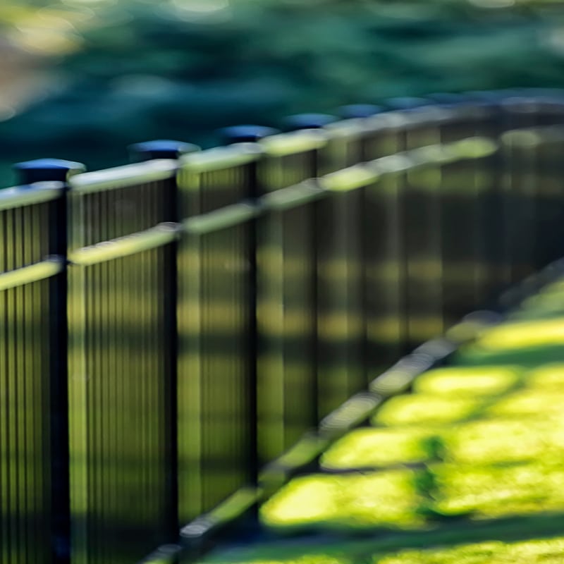 Clôture noire avec poteaux, flou artistique, verdure en arrière-plan. Ambiance paisible et esthétique minimaliste.