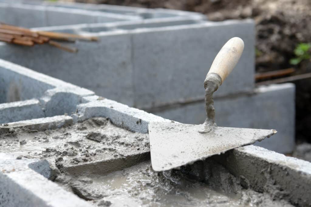 Maçonnerie en cours : truelle et mortier sur parpaings Truelle posée sur mortier frais au sommet de parpaings de béton, chantier de maçonnerie en cours. Blocs en arrière-plan.