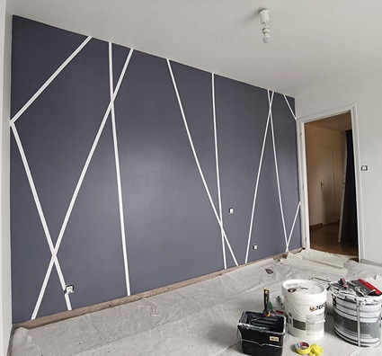 Mur gris anthracite avec motifs géométriques blancs. Rénovation intérieure, peinture, rouleau, pots de peinture au sol. Ambiance moderne.