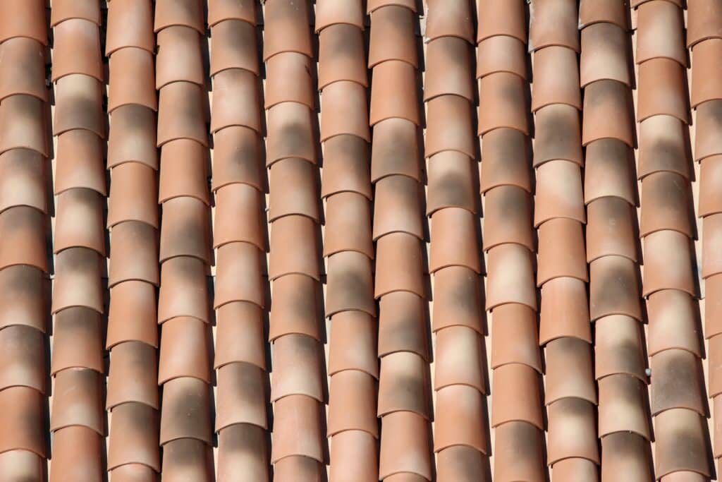 Rangées serrées de tuiles de toit en terre cuite courbes, formant un motif répétitif avec jeux d'ombre et lumière.