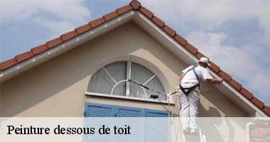 Peinture dessous de toit: Un peintre professionnel applique de la peinture sur le dessous du toit d'une maison beige avec des tuiles.